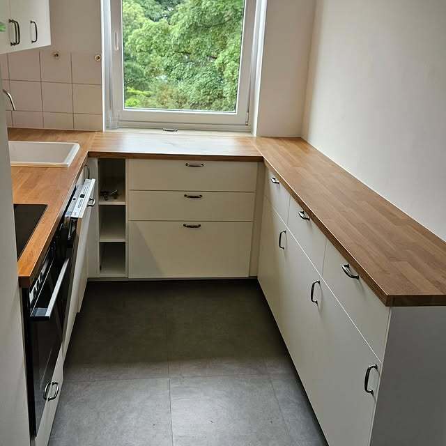 Weiße Küche mit Holzarbeitsplatte und großem Fenster