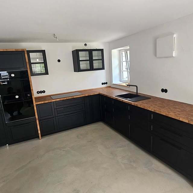 Schwarze L-Küche mit Holzarbeitsplatte und Glasvitrine